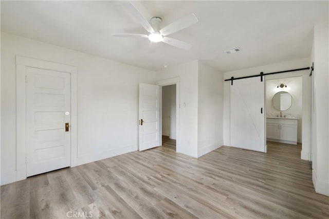 4415 12th St, Riverside, CA 92501 - unfurnished bedroom featuring a barn door, light wood-type flooring, baseboards, a ceiling fan, and connected bathroom