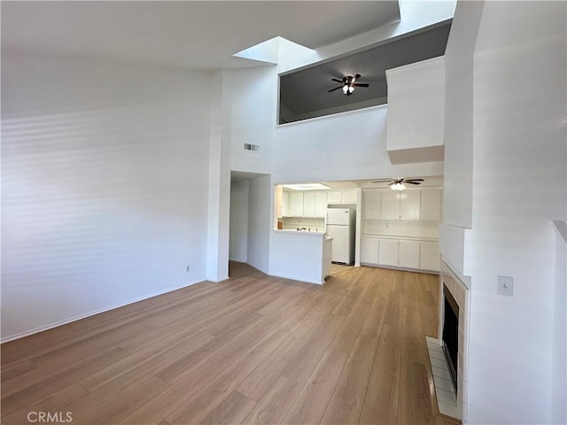 16521 Stonehaven Ct Unit 76, La Mirada, CA 90638 - unfurnished living room featuring ceiling fan, light wood-style floors, a high ceiling, a fireplace, and baseboards