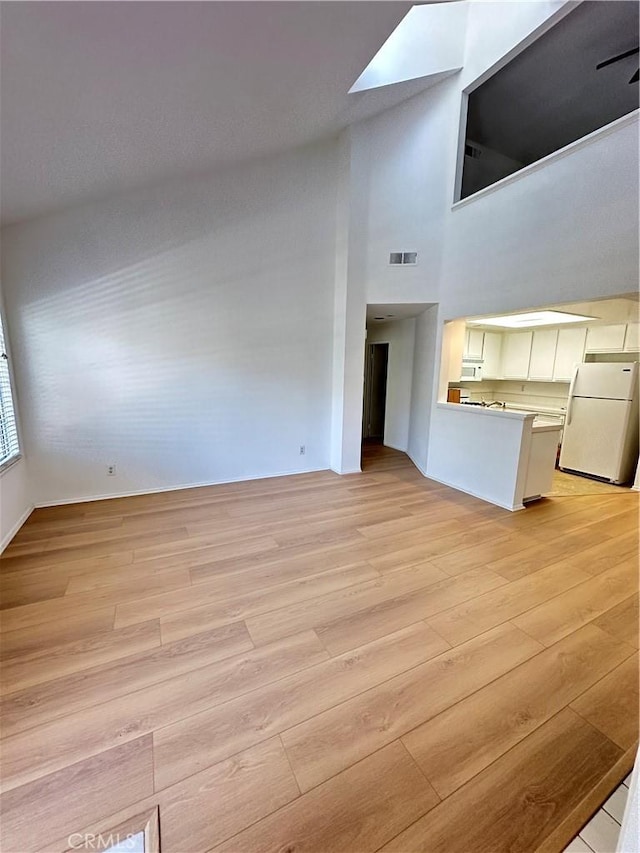 16521 Stonehaven Ct Unit 76, La Mirada, CA 90638 - unfurnished living room featuring light wood-type flooring, a skylight, and a towering ceiling