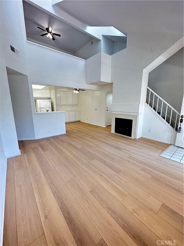 16521 Stonehaven Ct Unit 76, La Mirada, CA 90638 - unfurnished living room featuring ceiling fan, light wood finished floors, a fireplace with flush hearth, a high ceiling, and stairway