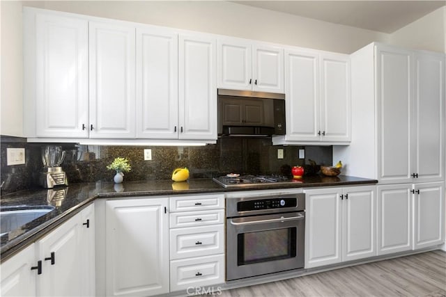 2911 Ballesteros Ln, Tustin, CA 92782 - kitchen featuring stainless steel appliances, white cabinetry, decorative backsplash, dark stone counters, and light wood-type flooring