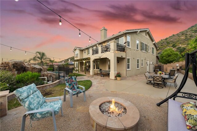 2514 Bulrush Cir, Corona, CA 92882 - back of house at dusk featuring a balcony, an outdoor fire pit, a patio area, a chimney, and stucco siding