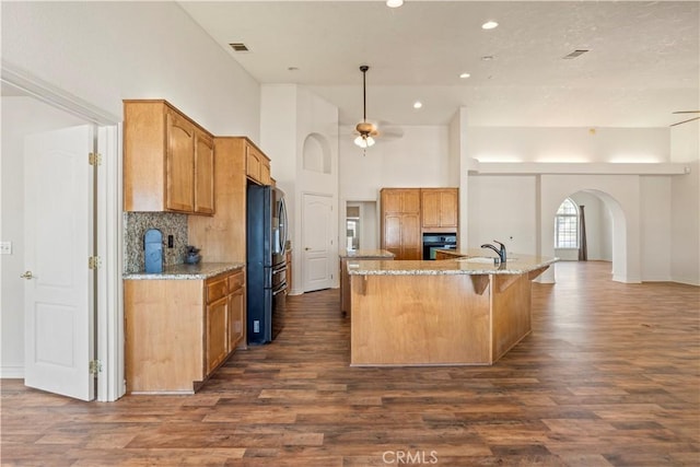 9098 Rattlesnake Rd, Phelan, CA 92371 - kitchen with freestanding refrigerator, arched walkways, a sink, dark wood finished floors, and an island with sink