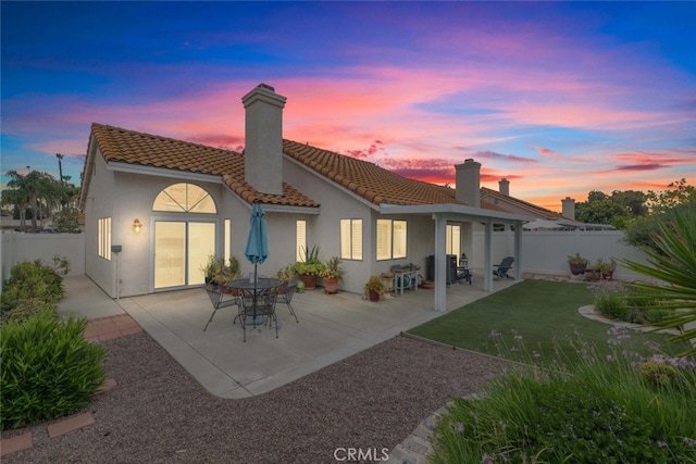 40280 Mimulus Way, Temecula, CA 92591 - back of house at dusk with a chimney, a tiled roof, a fenced backyard, stucco siding, and a patio