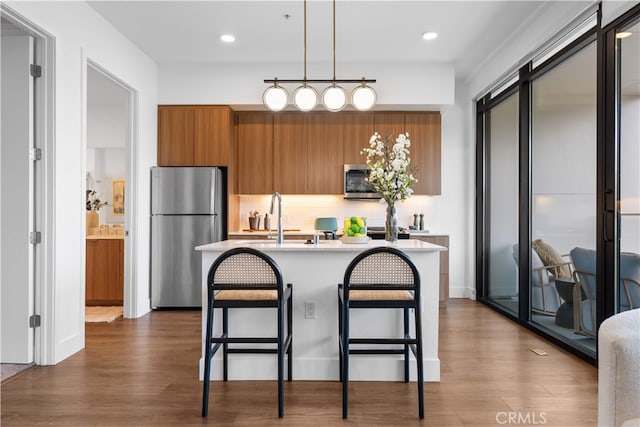 709 E Walnut St Unit 415, Pasadena, CA 91101 - kitchen featuring appliances with stainless steel finishes, brown cabinetry, light countertops, a breakfast bar, and dark wood-style flooring