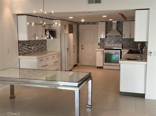 1553 Spyglass, Palm Springs, CA 92264 - kitchen with stainless steel range, wall chimney range hood, white fridge with ice dispenser, white cabinetry, and backsplash