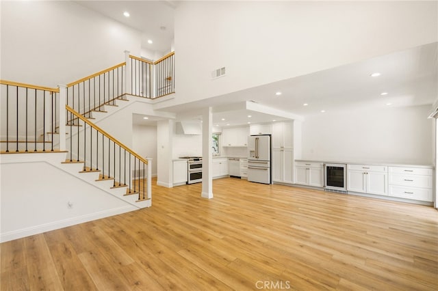 19464 Turtle Ridge Ln, Porter Ranch, CA 91326 - unfurnished living room featuring wine cooler, light wood-type flooring, stairs, a high ceiling, and recessed lighting