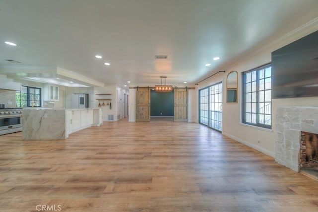 1043 Meadowview Ct, Corona, CA 92878 - unfurnished living room with a barn door, a stone fireplace, recessed lighting, light wood-style floors, and healthy amount of natural light