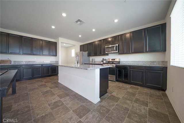 1172 Poinsettia Cir, Calimesa, CA 92320 - kitchen featuring stainless steel appliances, dark stone finish floors, a center island with sink, light stone counters, and dark brown cabinets