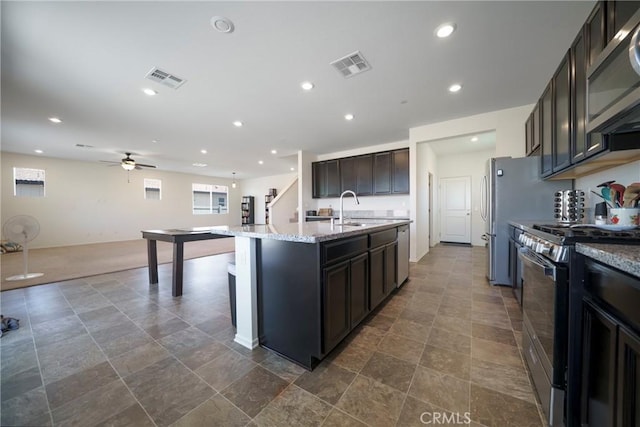 1172 Poinsettia Cir, Calimesa, CA 92320 - kitchen with appliances with stainless steel finishes, a ceiling fan, an island with sink, stone finish flooring, and light stone countertops