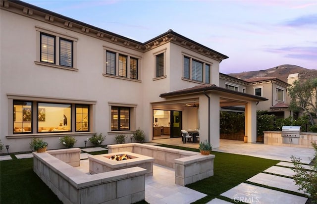 112 Mountain Sky, Irvine, CA 92602 - back of house at dusk with an outdoor fire pit, an outdoor kitchen, a patio, and stucco siding