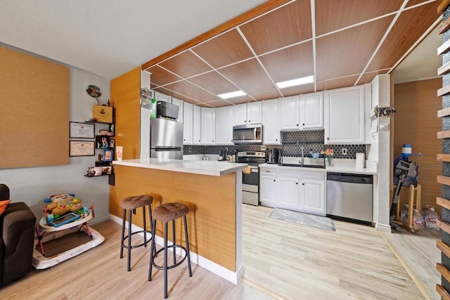 1845 Bayview Heights Dr Unit 110, San Diego, CA 92105 - kitchen with stainless steel appliances, light wood-type flooring, a breakfast bar area, a peninsula, and white cabinets