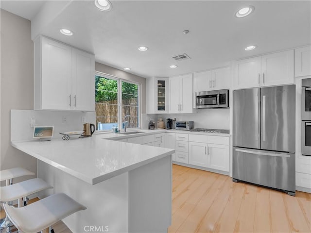 5637 Como Cir, Woodland Hills, CA 91367 - kitchen featuring appliances with stainless steel finishes, a peninsula, white cabinets, a kitchen bar, and light wood-type flooring