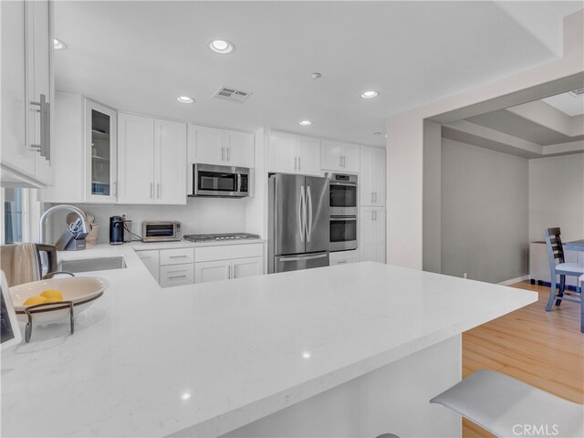 5637 Como Cir, Woodland Hills, CA 91367 - kitchen featuring appliances with stainless steel finishes, glass insert cabinets, recessed lighting, white cabinets, and a peninsula