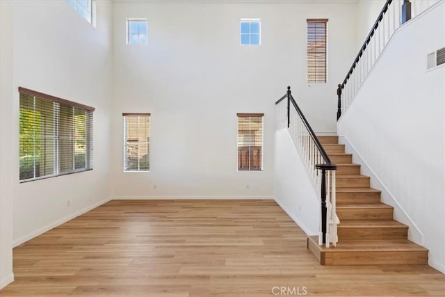 21567 Coral Rock Ln, Wildomar, CA 92595 - unfurnished living room with a towering ceiling, stairs, light wood-style floors, and baseboards
