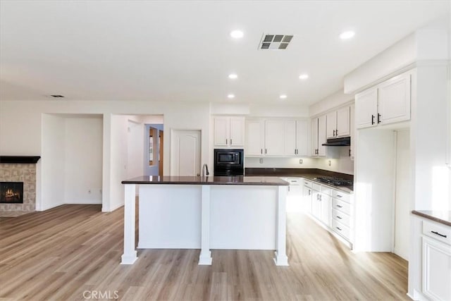 21567 Coral Rock Ln, Wildomar, CA 92595 - kitchen featuring under cabinet range hood, black appliances, dark countertops, white cabinets, and light wood-style floors