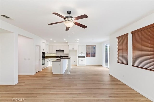 21567 Coral Rock Ln, Wildomar, CA 92595 - kitchen with dark countertops, open floor plan, ceiling fan, white cabinetry, and light wood finished floors