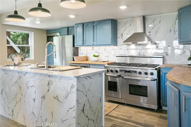 22060 Mockingbird Ln, Cedarpines Park, CA 92322 - kitchen featuring range with two ovens, wall chimney exhaust hood, blue cabinets, freestanding refrigerator, and backsplash