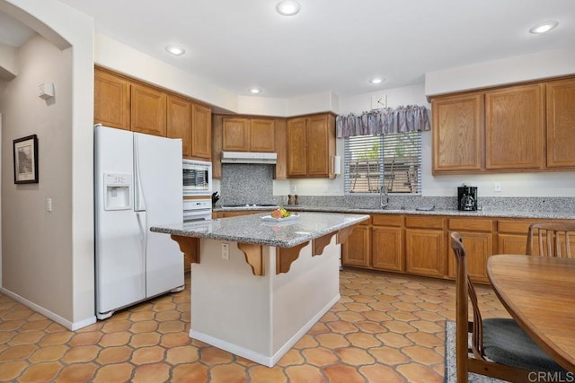 31135 Gleneagles Dr, Temecula, CA 92591 - kitchen with white refrigerator with ice dispenser, under cabinet range hood, stainless steel microwave, light stone countertops, and a breakfast bar