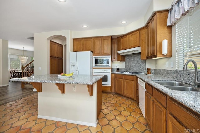 31135 Gleneagles Dr, Temecula, CA 92591 - kitchen with white appliances, under cabinet range hood, brown cabinetry, a breakfast bar, and a center island