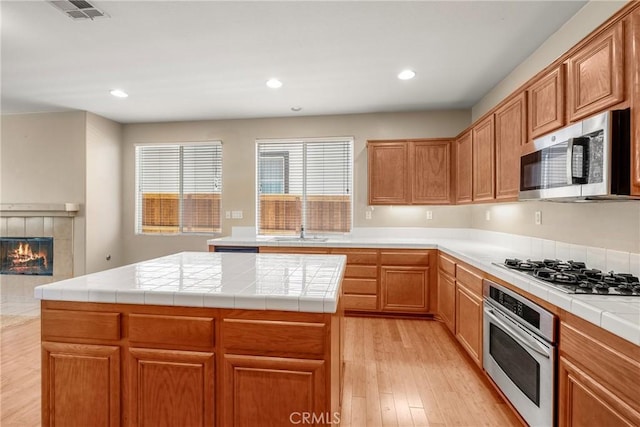33010 Poppy St, Temecula, CA 92592 - kitchen with appliances with stainless steel finishes, light wood finished floors, a sink, a tiled fireplace, and a center island