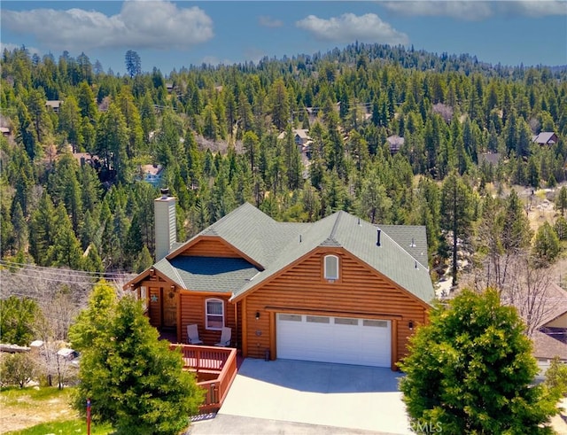 26855 Inyo Ct, Lake Arrowhead, CA 92352 - view of front of home with a forest view, concrete driveway, an attached garage, a chimney, and a shingled roof