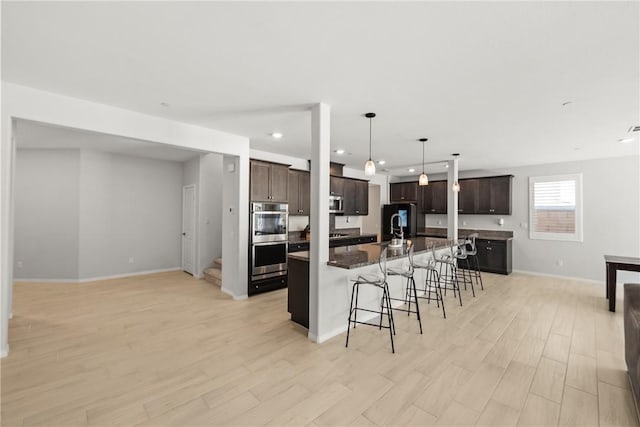 33168 Toledo Bend Ct, Winchester, CA 92596 - kitchen with a breakfast bar, appliances with stainless steel finishes, dark brown cabinets, a large island with sink, and recessed lighting