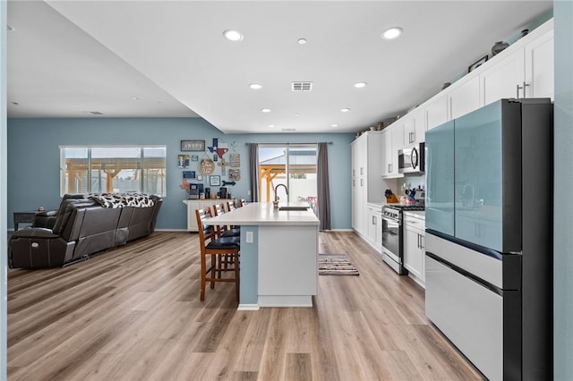 1372 Bello Pl, San Jacinto, CA 92582 - kitchen with stainless steel appliances, a sink, light wood-style flooring, white cabinetry, and a center island with sink