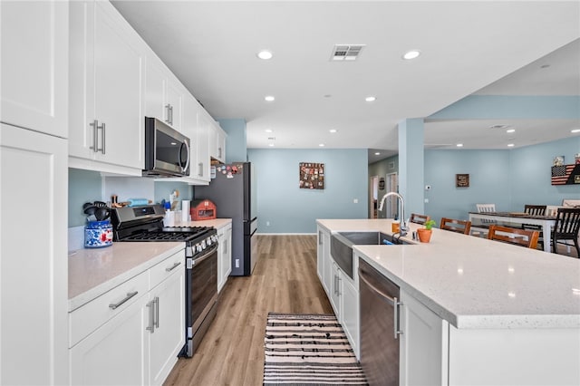 1372 Bello Pl, San Jacinto, CA 92582 - kitchen featuring stainless steel appliances, a sink, an island with sink, white cabinets, and light wood finished floors
