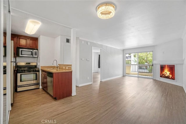 5500 Owensmouth Ave Unit 218, Woodland Hills, CA 91367 - kitchen featuring stainless steel appliances, open floor plan, a sink, light wood finished floors, and a lit fireplace