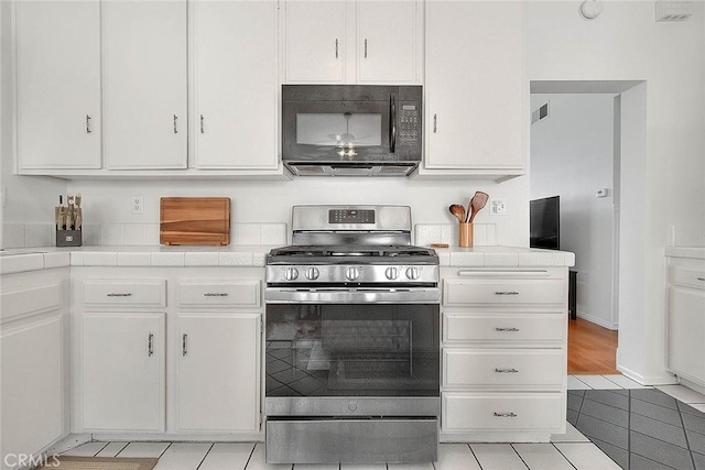 22784 Wren St, Grand Terrace, CA 92313 - kitchen featuring stainless steel range with gas stovetop, black microwave, tile countertops, white cabinets, and light tile patterned floors