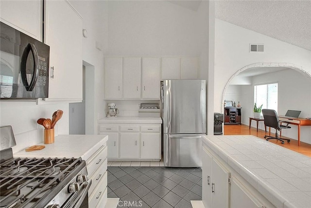 22784 Wren St, Grand Terrace, CA 92313 - kitchen featuring appliances with stainless steel finishes, tile countertops, white cabinetry, vaulted ceiling, and tile patterned flooring