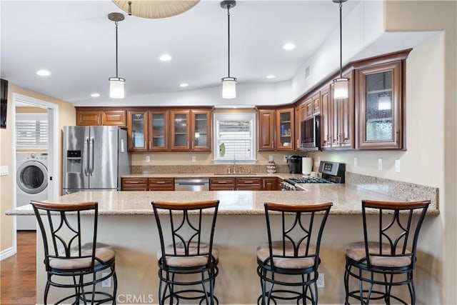 249 Loyola Rd, Costa Mesa, CA 92626 - kitchen with washer / dryer, appliances with stainless steel finishes, brown cabinetry, a sink, and a peninsula