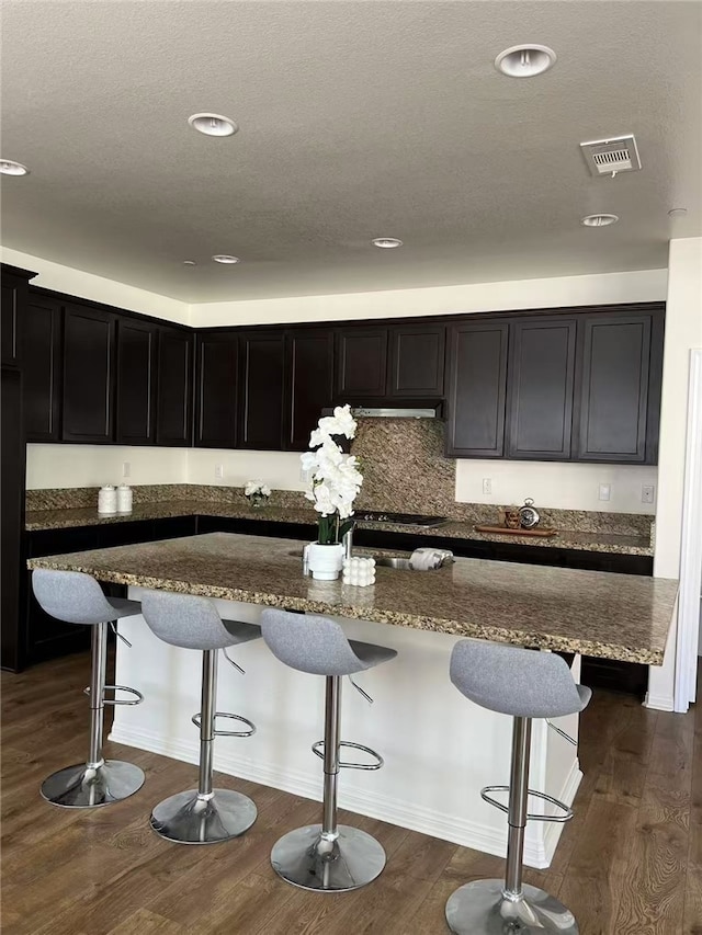7739 Lupin St, Chino, CA 91708 - kitchen with dark stone counters, dark cabinets, a breakfast bar, dark wood-type flooring, and a kitchen island with sink
