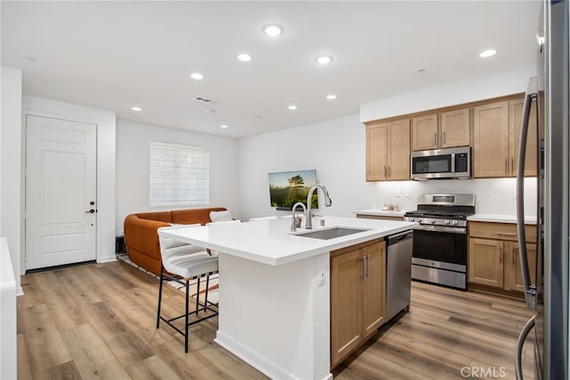 39376 Corvina Ln, Temecula, CA 92591 - kitchen with appliances with stainless steel finishes, a sink, open floor plan, a kitchen island with sink, and light wood-style floors
