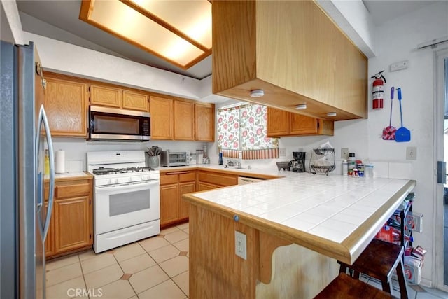 24880 Balestrieri Rd, Hemet, CA 92544 - kitchen with stainless steel appliances, a peninsula, light tile patterned floors, a breakfast bar, and tile countertops