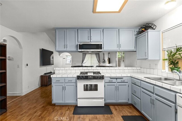 258 Vail Dr, Chico, CA 95973 - kitchen featuring stainless steel microwave, white range with gas stovetop, a peninsula, tile counters, and arched walkways