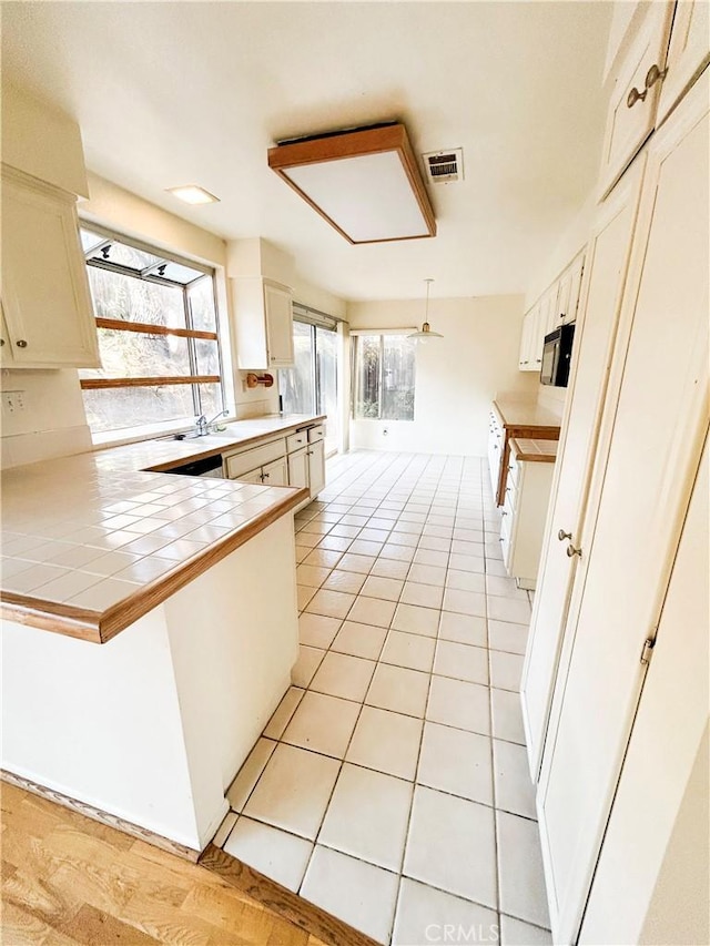 23878 Bouquet Canyon Pl, Moreno Valley, CA 92557 - kitchen with black microwave, tile countertops, a peninsula, light tile patterned floors, and decorative light fixtures