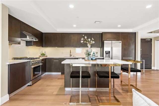 2939 Leeward Ave Unit 415, Los Angeles, CA 90005 - kitchen with appliances with stainless steel finishes, ventilation hood, dark brown cabinetry, a sink, and light wood-style flooring