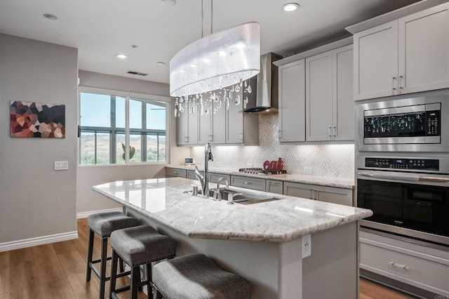 1139 Prussian, Oceanside, CA 92057 - kitchen featuring appliances with stainless steel finishes, wall chimney range hood, backsplash, light wood-type flooring, and a center island with sink