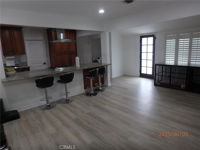 17457 Covello St, Van Nuys, CA 91406 - kitchen featuring wall chimney range hood, a breakfast bar area, light wood-style flooring, light stone counters, and recessed lighting