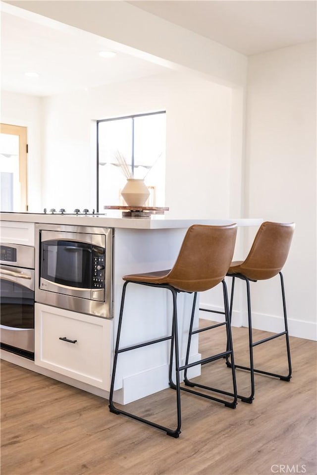 63326 Sunny Sands Dr, Joshua Tree, CA 92252 - kitchen with appliances with stainless steel finishes, white cabinets, a breakfast bar area, light wood-type flooring, and baseboards