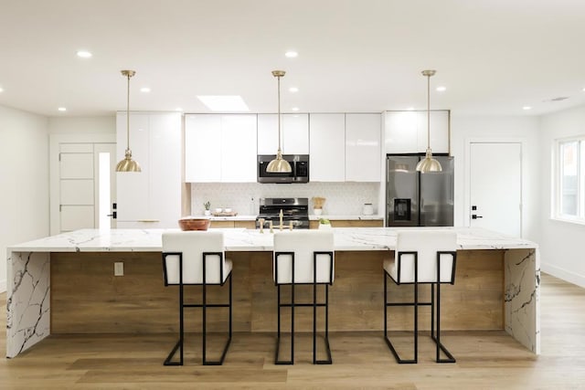 4380 Rolfe Rd, San Diego, CA 92117 - kitchen with stainless steel appliances, a spacious island, white cabinets, light wood-type flooring, and decorative backsplash