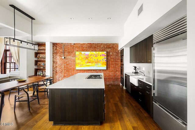 940 E 2nd St Unit 37, Los Angeles, CA 90012 - kitchen with appliances with stainless steel finishes, light countertops, brick wall, a center island, and dark wood-type flooring