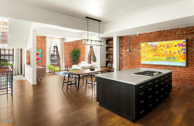 940 E 2nd St Unit 37, Los Angeles, CA 90012 - kitchen with brick wall, dark cabinetry, dark wood-style flooring, light countertops, and a kitchen island