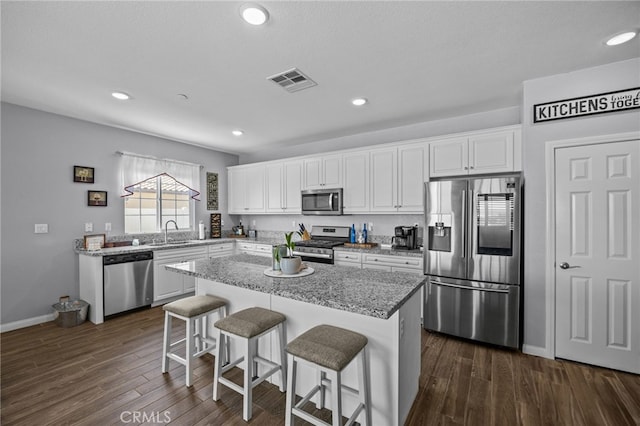 24909 Miners View Ln, Moreno Valley, CA 92557 - kitchen with appliances with stainless steel finishes, white cabinetry, a breakfast bar, a kitchen island, and dark wood-style floors