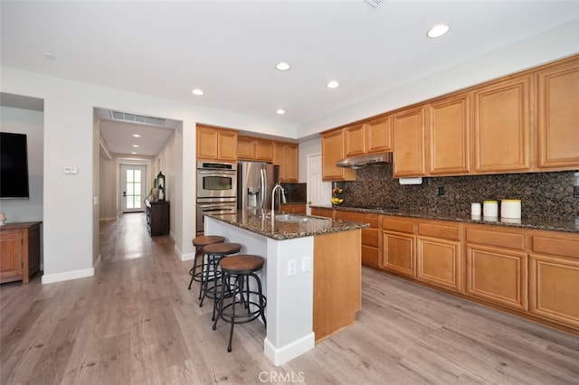 28978 Williston Ct, Temecula, CA 92591 - kitchen featuring stainless steel appliances, under cabinet range hood, light wood-style floors, a breakfast bar, and dark stone countertops