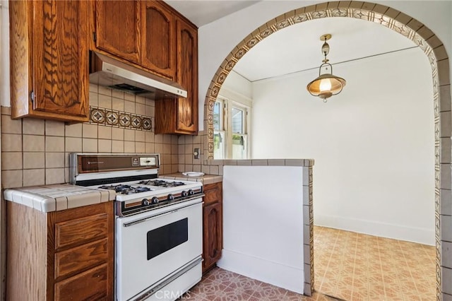 542 Ojai Rd, Santa Paula, CA 93060 - kitchen featuring white gas stove, under cabinet range hood, tile counters, decorative backsplash, and brown cabinets