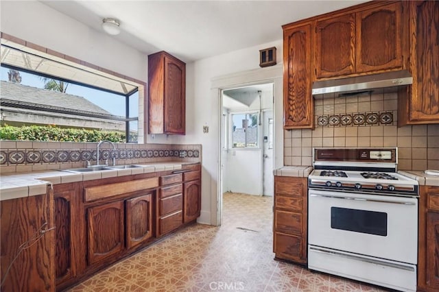 542 Ojai Rd, Santa Paula, CA 93060 - kitchen with white range with gas cooktop, under cabinet range hood, tile countertops, backsplash, and light flooring