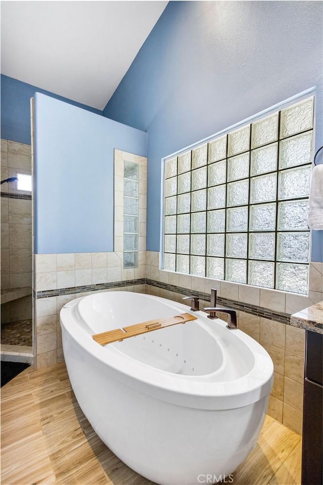 3475 Paseo Verde Ave, Merced, CA 95348 - bathroom with tile walls, a jetted tub, vaulted ceiling, a tile shower, and wood finished floors